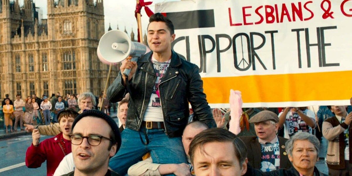 Un jeune homme parlant dans un mégaphone alors qu'il est porté par une foule dans le film Pride.
