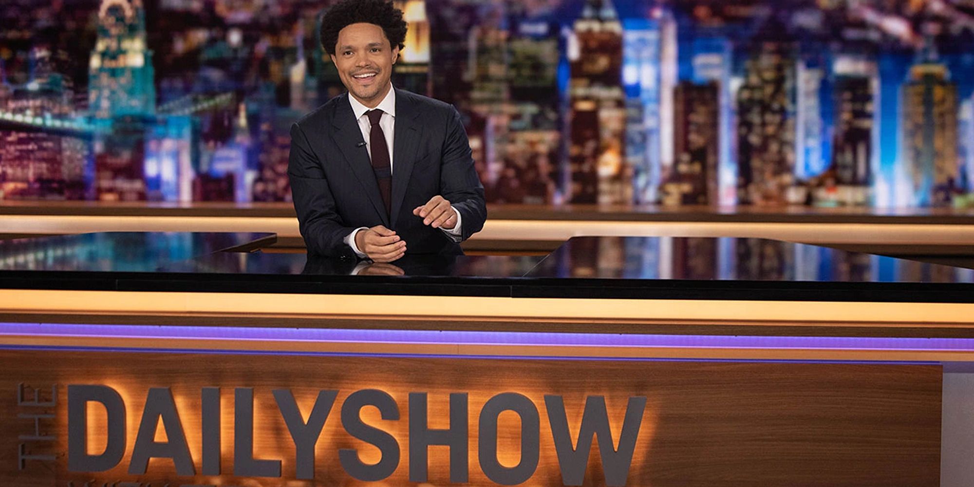 Trevor Noah behind a desk that reads