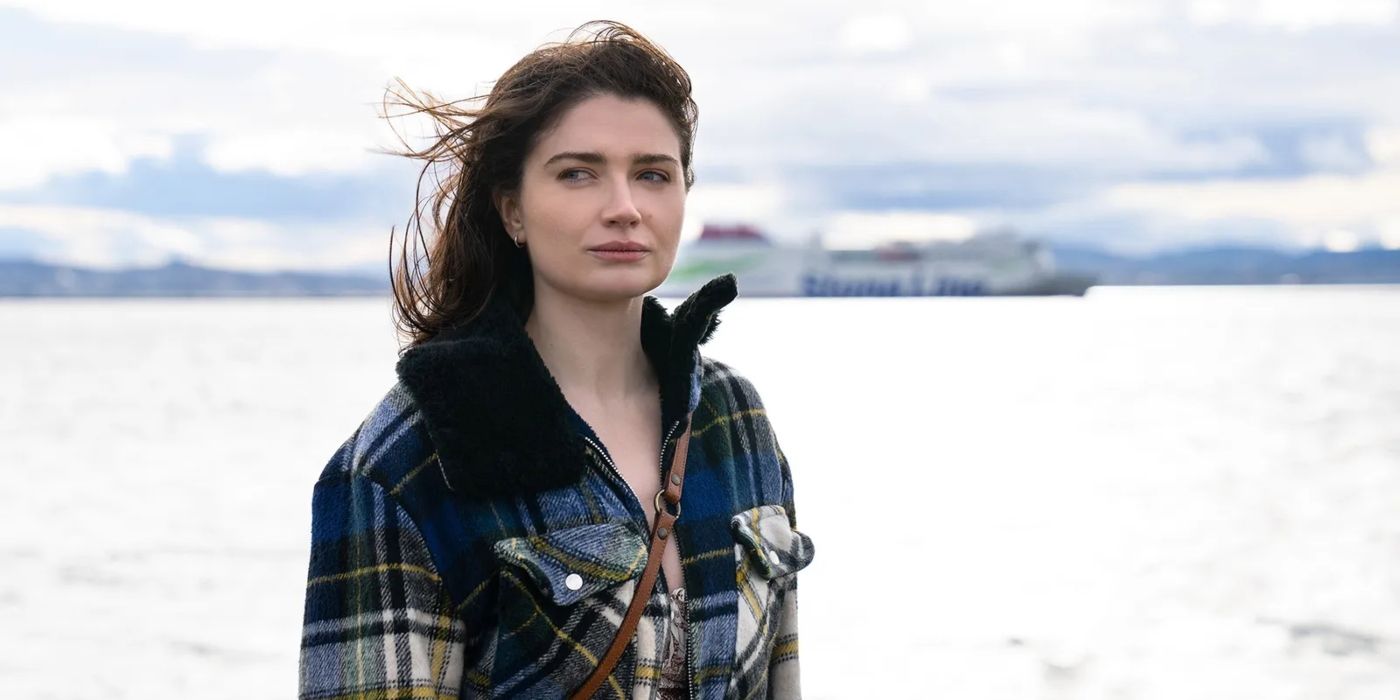 Becka Garvey (Eve Hewson) se tient devant l'océan dans un manteau à carreaux, les cheveux au vent dans une scène de 