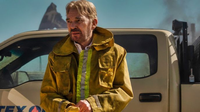 Billy Bob Thornton standing in front of a truck with a work jacket on