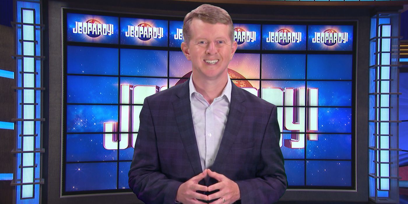 Ken Jennings souriant et debout devant le plateau de jeu sur Jeopardy ! parler à la caméra