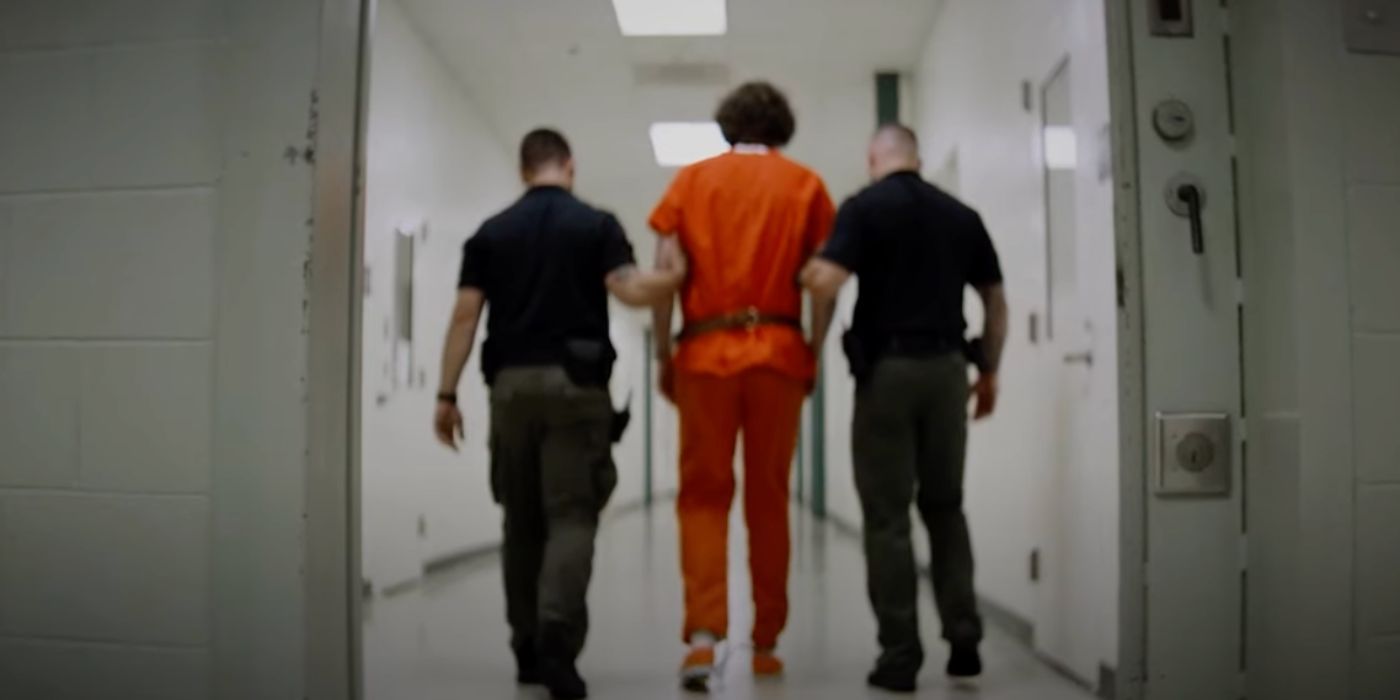 two police officers walk a prisoner dressed in orange down a corridor