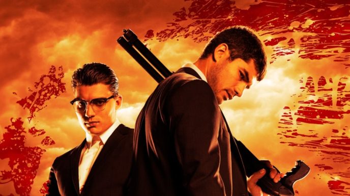 Seth Gecko (D. J. Cotrona) standing with a rifle slung over his shoulder with his brother Richie (Zane Holtz) standing behind him against an orange backdrop for From Dusk Till Dawn: The Series