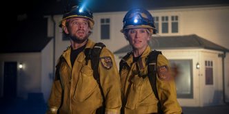 Max Thieriot and Leven Rambin standing in front of a house in firefighting gear