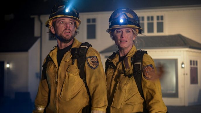 Max Thieriot and Leven Rambin standing in front of a house in firefighting gear