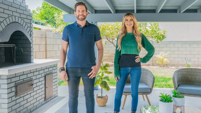 Tarek El Moussa and Christina Hall posing by an outside pizza oven in a patio